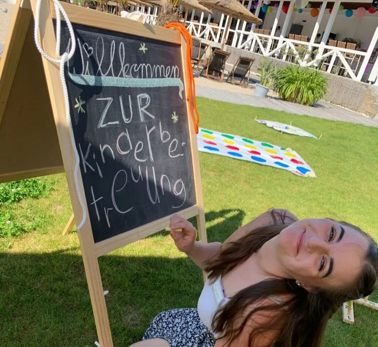 Kinderanimateurin beschriftet Kreidetafel für Kinderbereich und lächelt in die Kamera